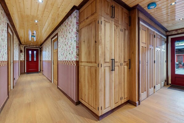 Un pasillo con suelo de madera, una puerta roja al final y armarios de madera a lo largo de las paredes.