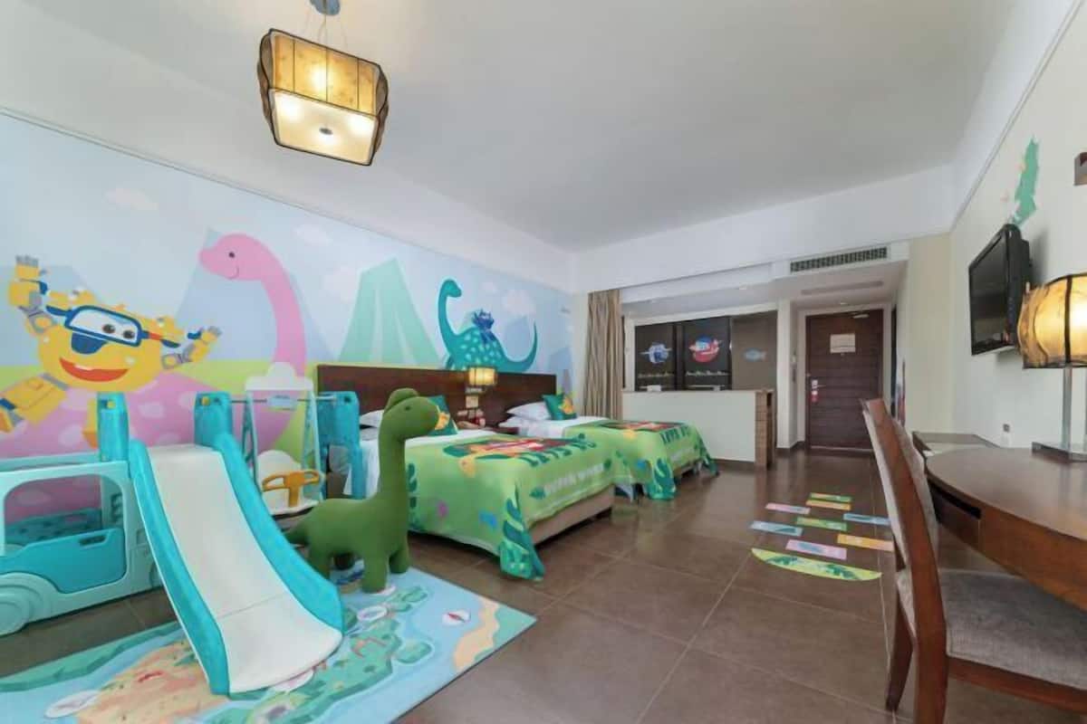 Ein Kinderzimmer mit Rutsche, Dino-Themen-Bettwäsche und Wandgemälde.