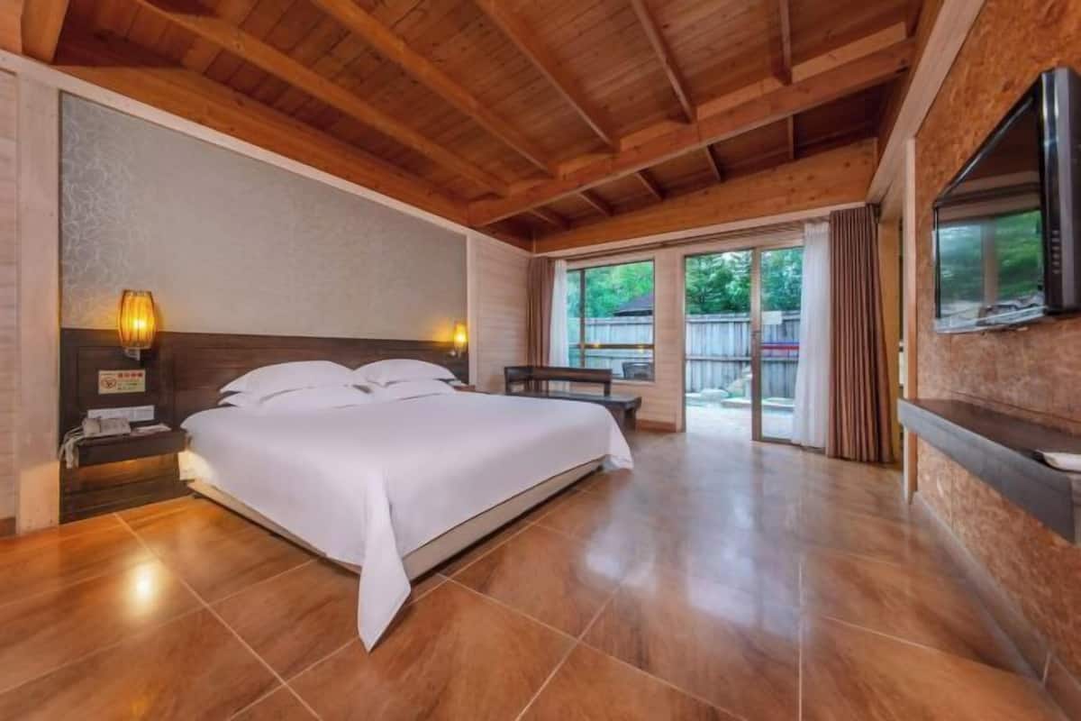 Ein Schlafzimmer mit einem großen Bett, Holzboden und einem an der Wand befestigten Fernseher.