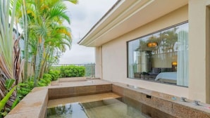 Een wellnessruimte met een jacuzzi, omringd door groen en een glazen wand met uitzicht op het interieur.