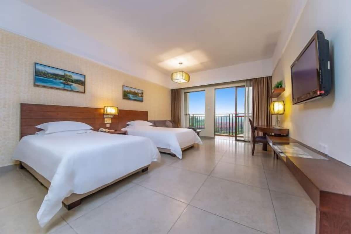 Ein Hotelzimmer mit zwei Betten, einem Fernseher, einem Schreibtisch und einem Balkon mit Aussicht.