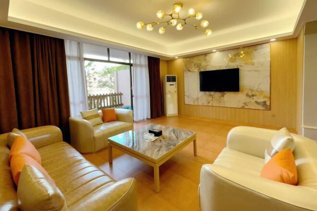 Ein geräumiges Wohnzimmer mit Ledersofas, einem Marmortisch und einem flachbildfernseher, der an einer Marmorwand angebracht ist.