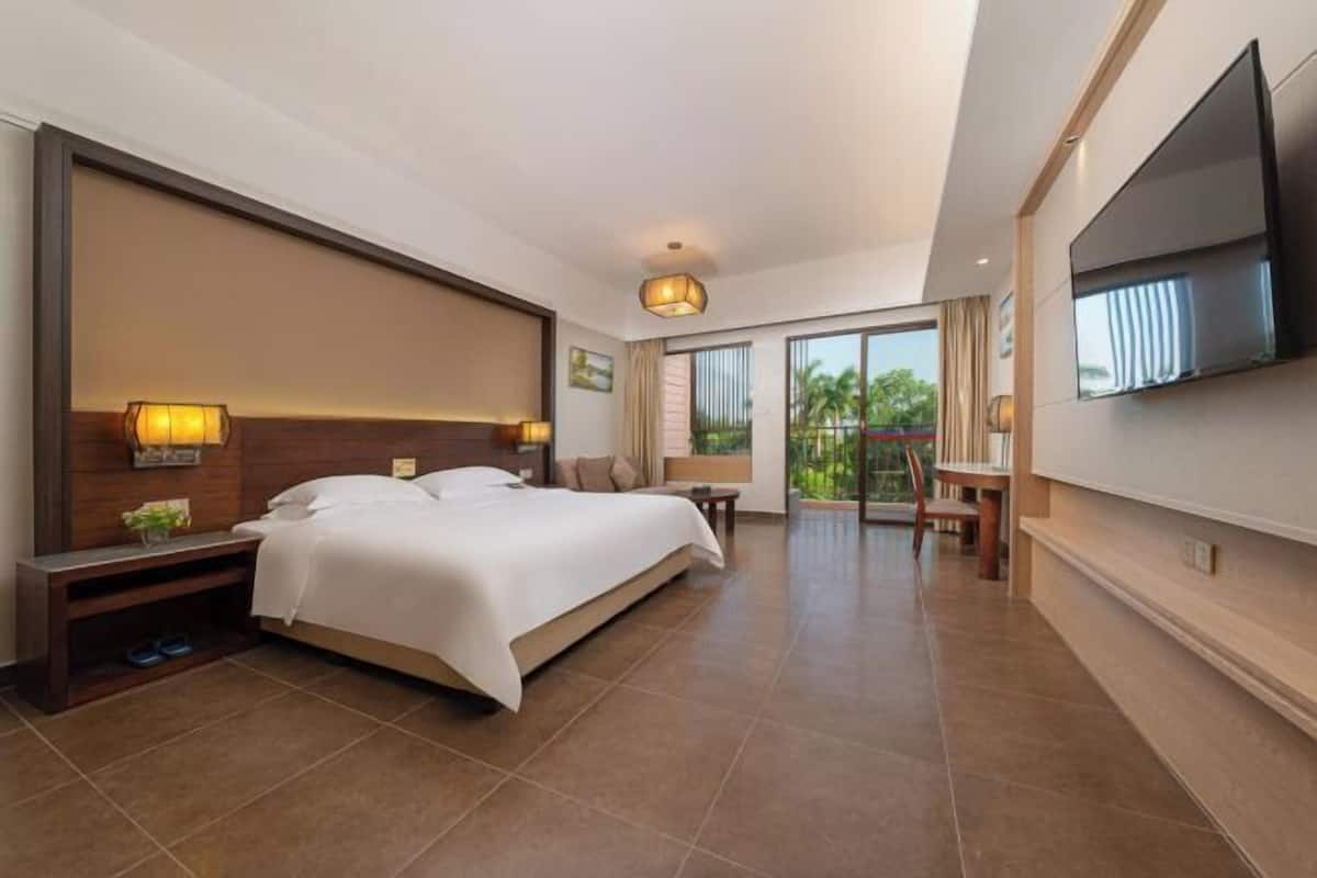 Ein Hotelzimmer mit einem großen Bett, einem Schreibtisch, einem Fernseher und einem Balkon mit Blick.