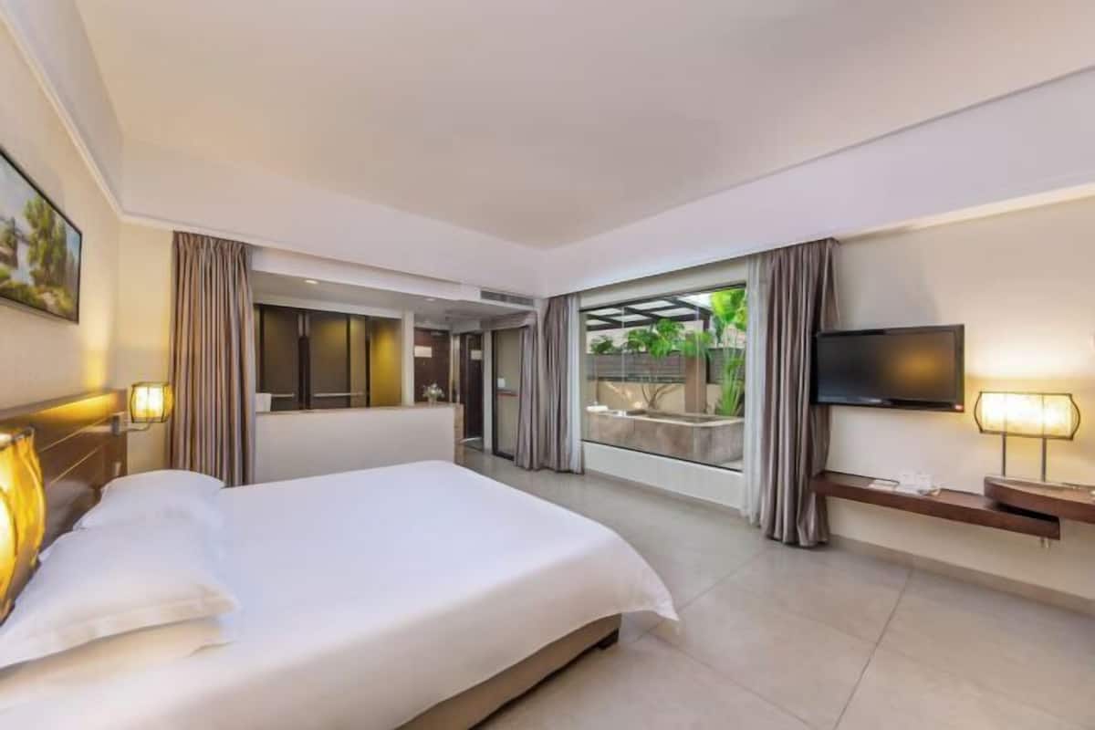 Ein modernes Hotelzimmer mit einem großen Bett, einem Flachbildfernseher und einem Balkon mit Blick auf Grünflächen.