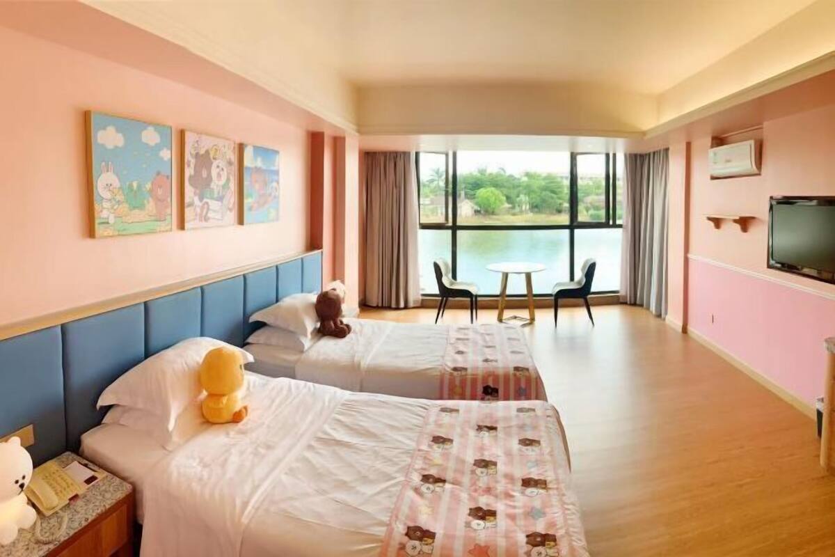 Ein Hotelzimmer mit zwei Betten, einem großen Fenster mit Blick auf Grünflächen, einem Fernseher und einem Tisch mit Stühlen.