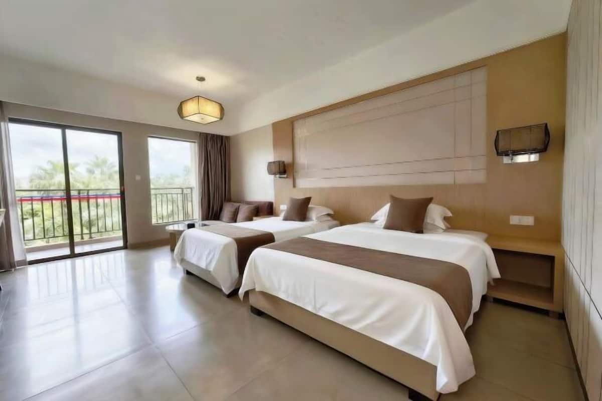 Ein Hotelzimmer mit zwei Betten, einer großen Schiebetür zum Balkon, einer Deckenleuchte und einem an der Wand befestigten Regal.