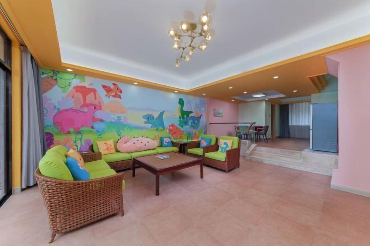 A spacious living area with a mural of dinosaurs, green sofas, and a chandelier.