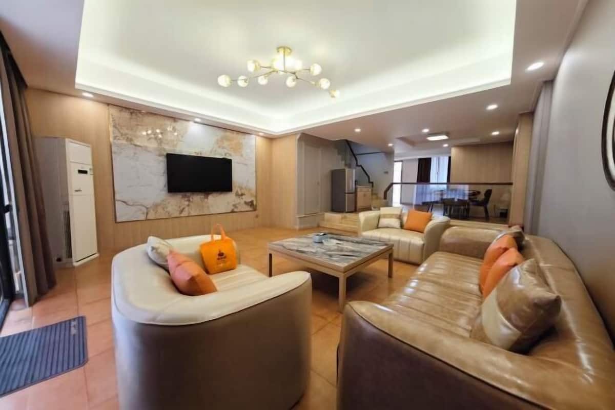 Ein modernes Wohnzimmer mit einem Flachbildfernseher, Ledersofas, einer Wand mit Marmorverkleidung und einer Treppe, die in eine obere Ebene führt.