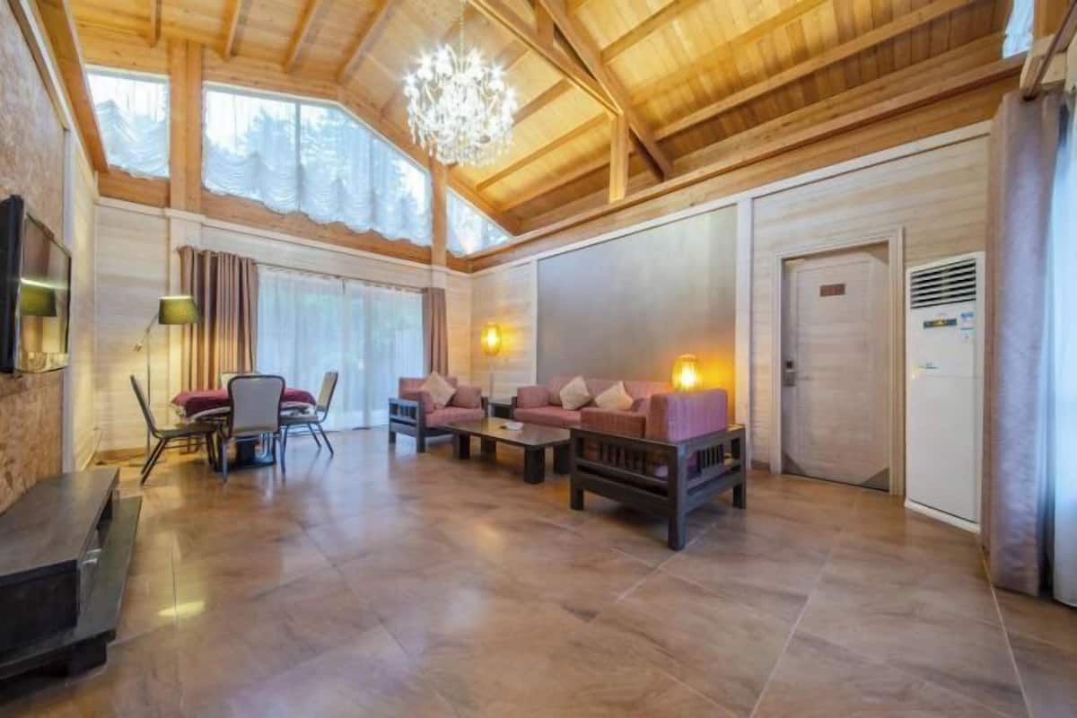 Ein geräumiger Raum mit Holzbalken, einem Chandelier und einem Kamin. Zwei Sofas und ein Esstisch mit Stühlen sind vorhanden.