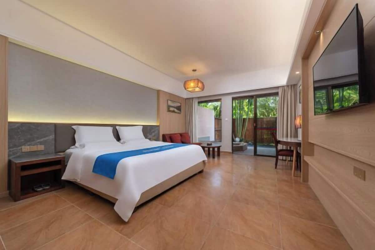 Ein Hotelzimmer mit einem großen Bett, einem Schreibtisch, einem Sessel, einem Fernseher und einer Schiebetür zum Balkon.