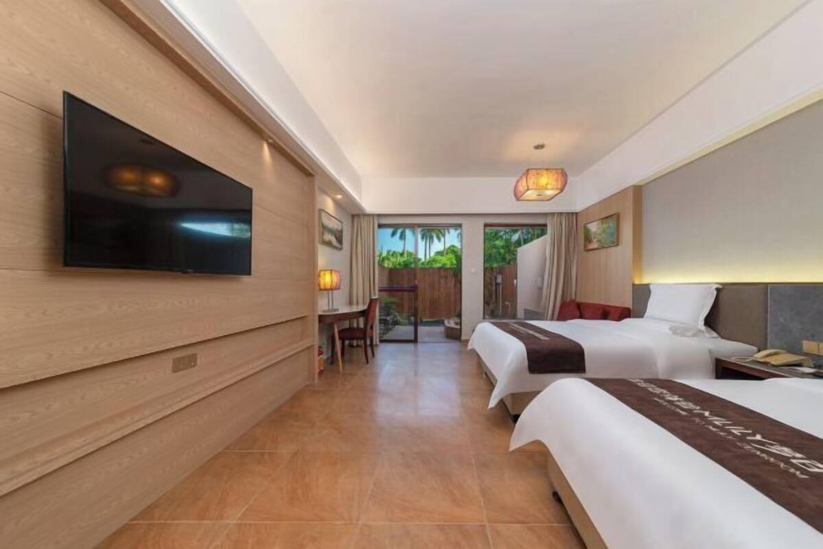 Ein Hotelzimmer mit Flachbildfernseher, zwei Betten, einem Schreibtisch und Blick auf Grünflächen.