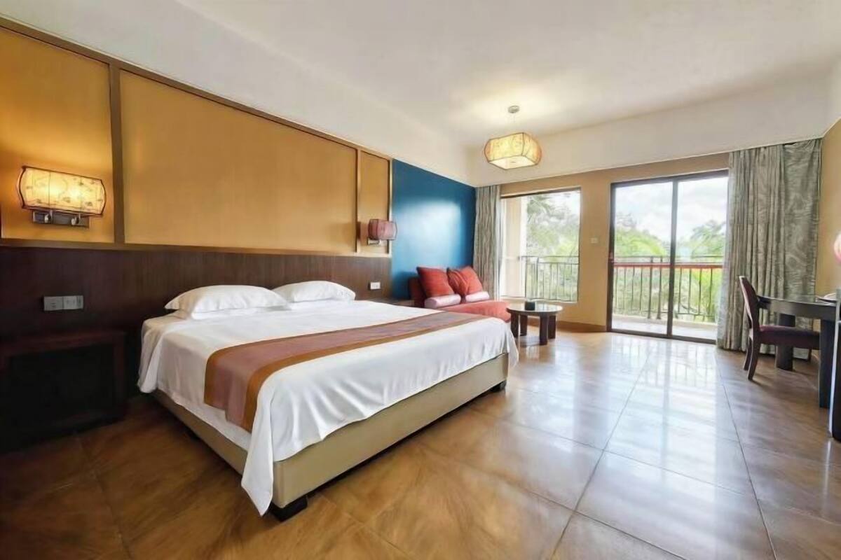 Ein Hotelzimmer mit einem großen Bett, einem kleinen Tisch, einem Stuhl und einem Balkon mit Blick.