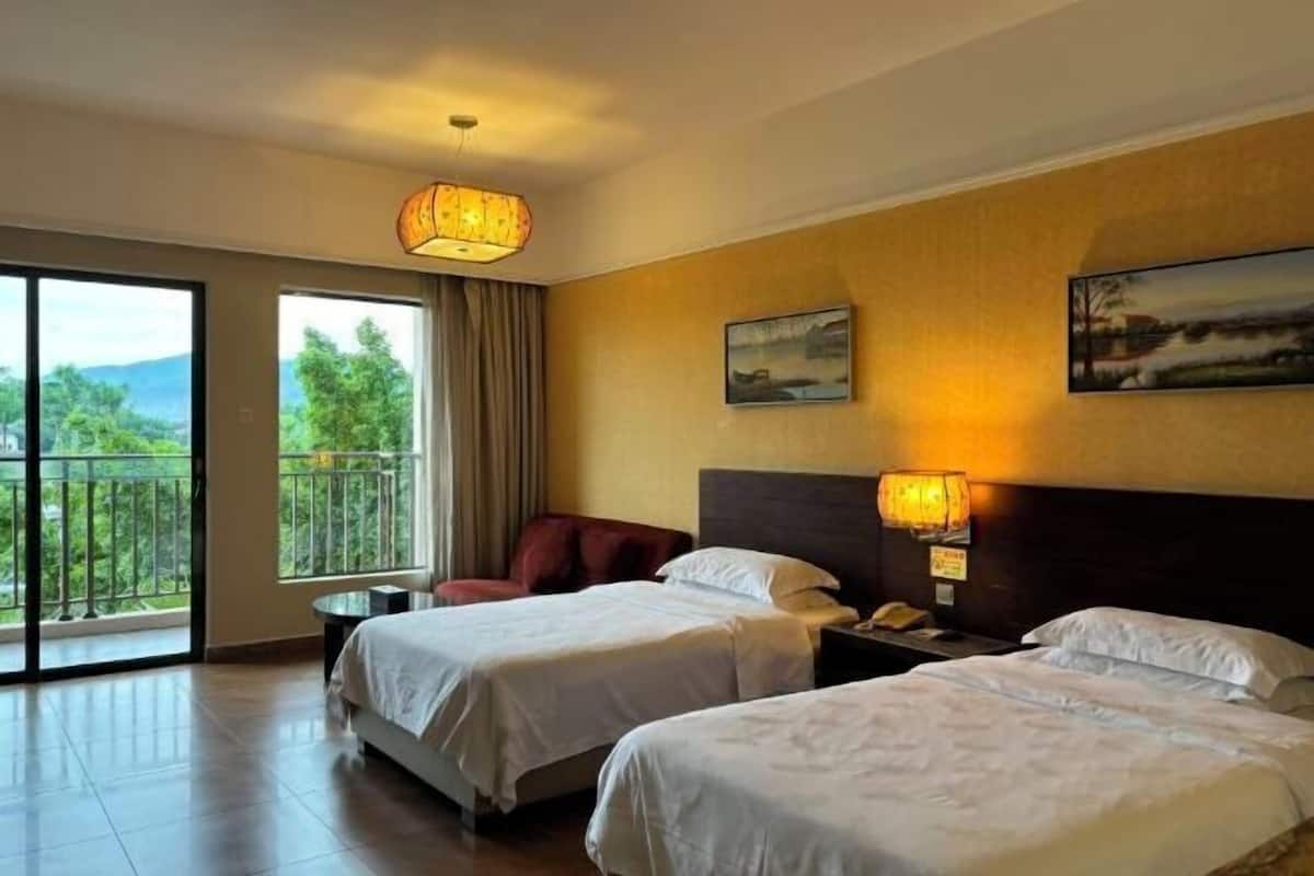 Ein Hotelzimmer mit zwei Betten, einem Balkon mit Blick auf Grünflächen und einem Bild an der Wand.