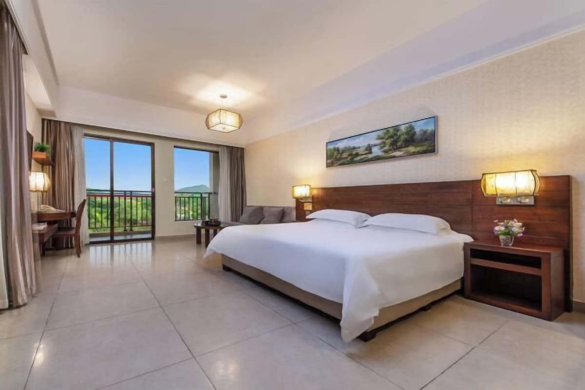 A spacious hotel room with a large bed, a desk, and a balcony with a view.