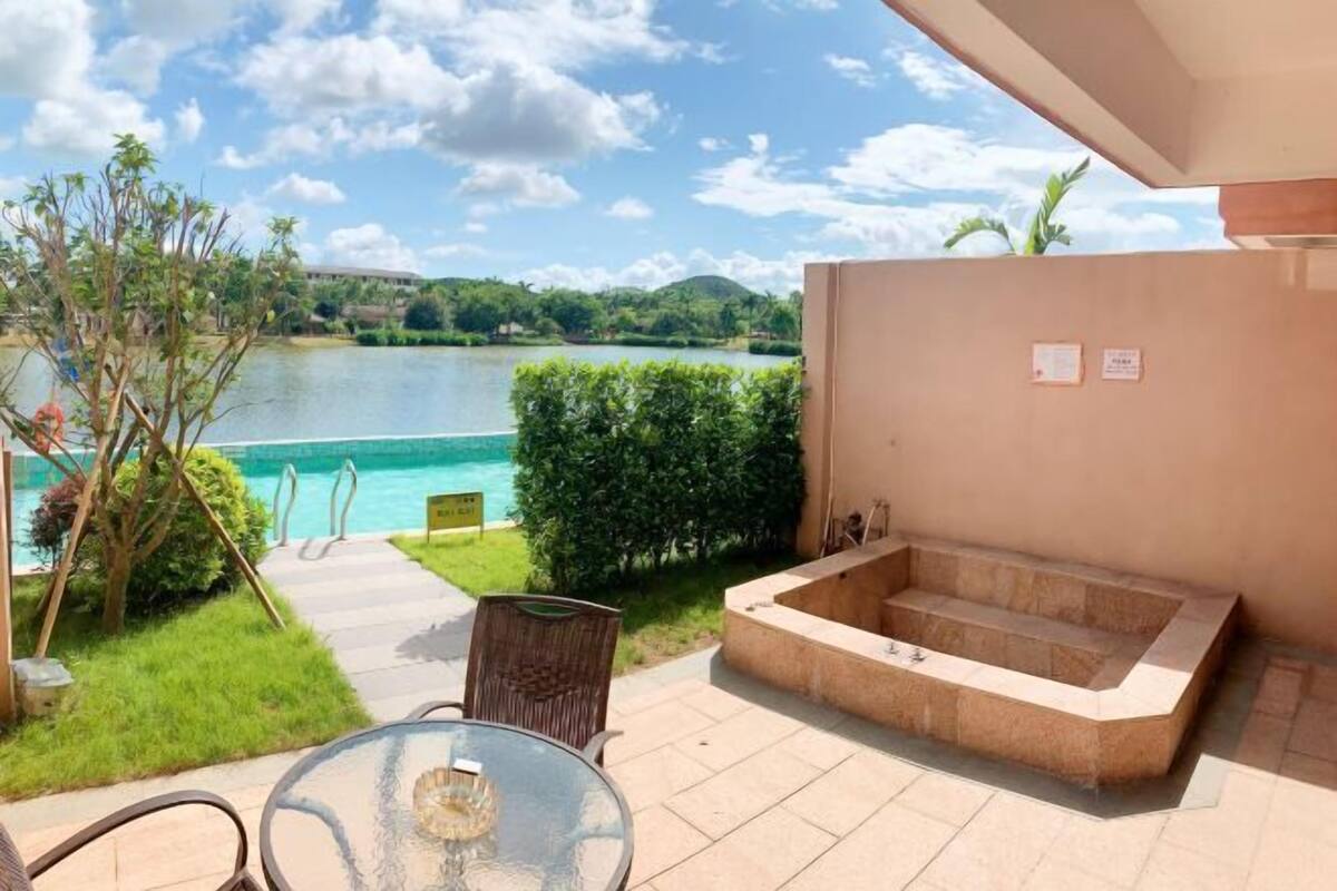 Eine Terrasse mit Glastisch und Stühlen, einem Whirlpool und Blick auf einen See.