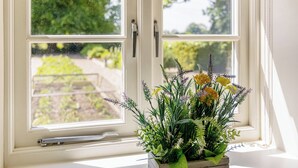 A window with a view of a garden, a window blind, and a potted plant with greenery and flowers. - Rosemary – Ground Floor (Boston)
