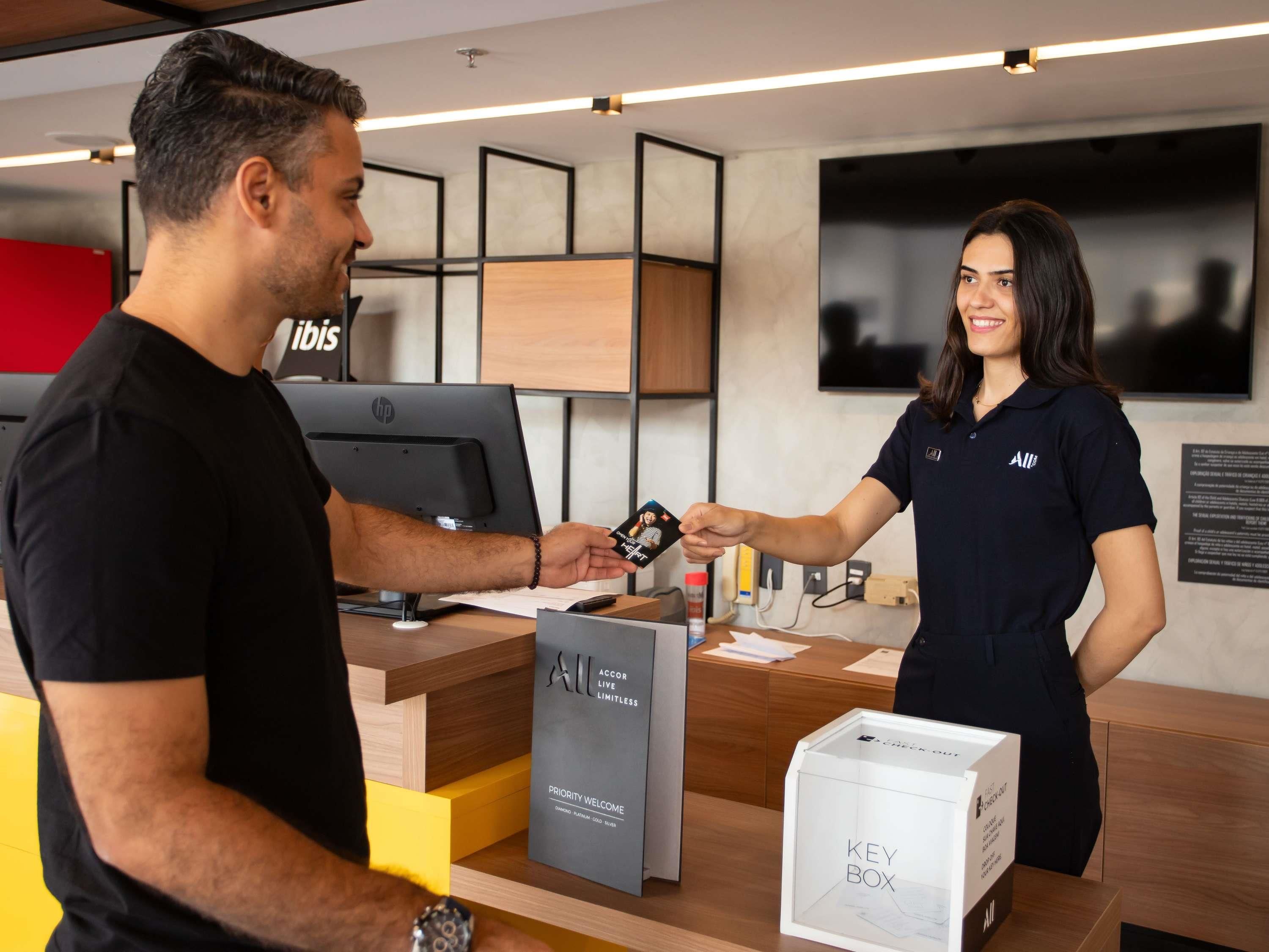 Uma receção de hotel com um computador, um sinal de boas-vindas prioritárias e uma caixa de chaves.