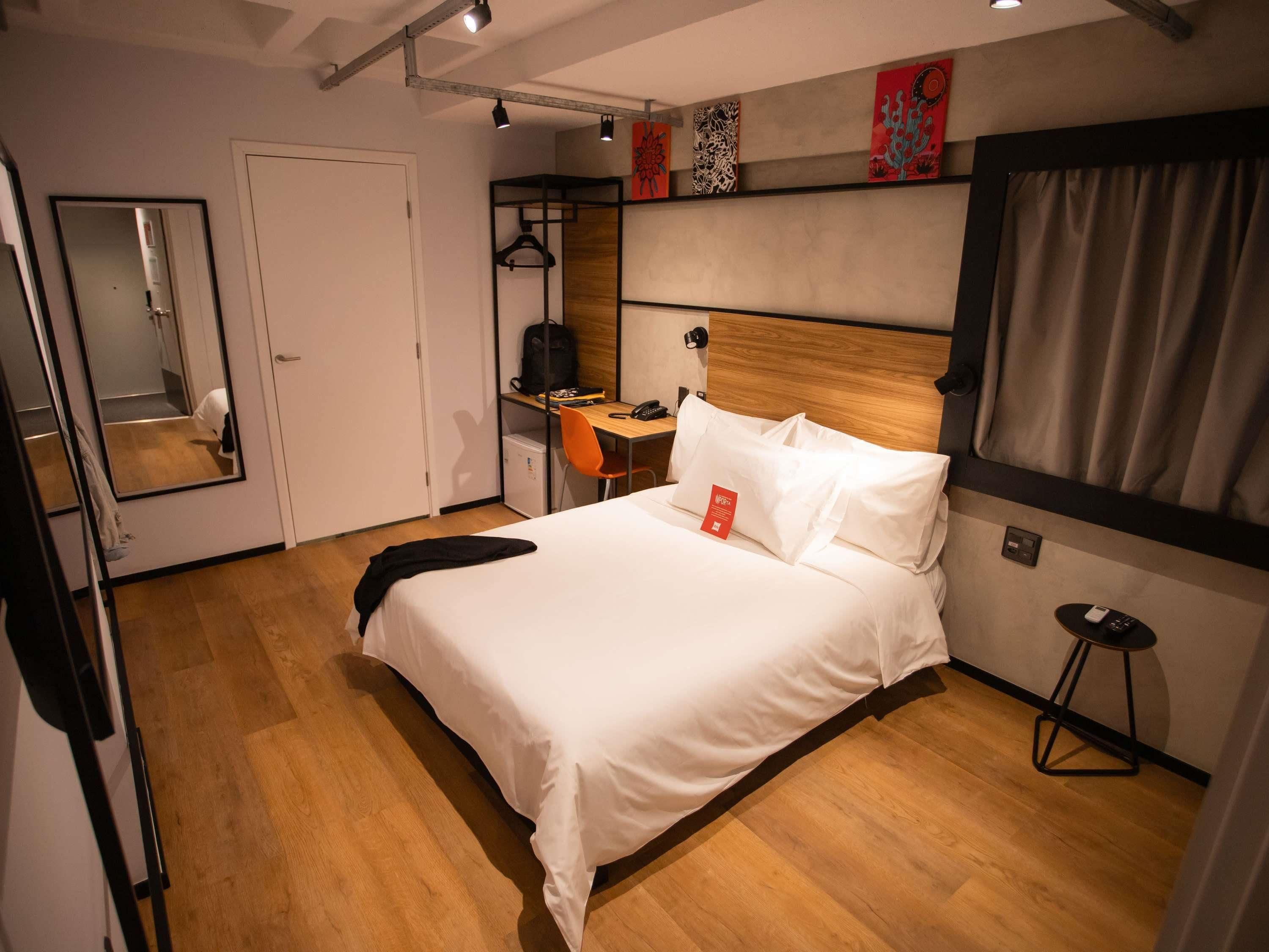 A hotel room with a bed, a desk, a chair, a mirror, and a wardrobe.