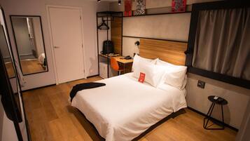 A hotel room with a bed, a desk, a chair, a mirror, and a wardrobe.