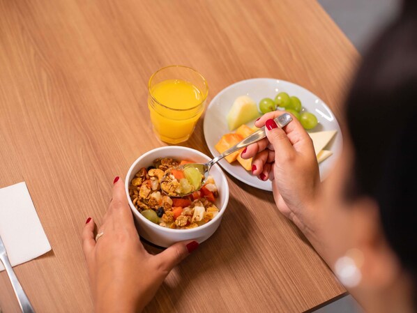 A person eating cereal with a spoon, a glass of orange juice, and a plate with grapes and melon. - Ibis Serra Talhada (Serra Talhada)