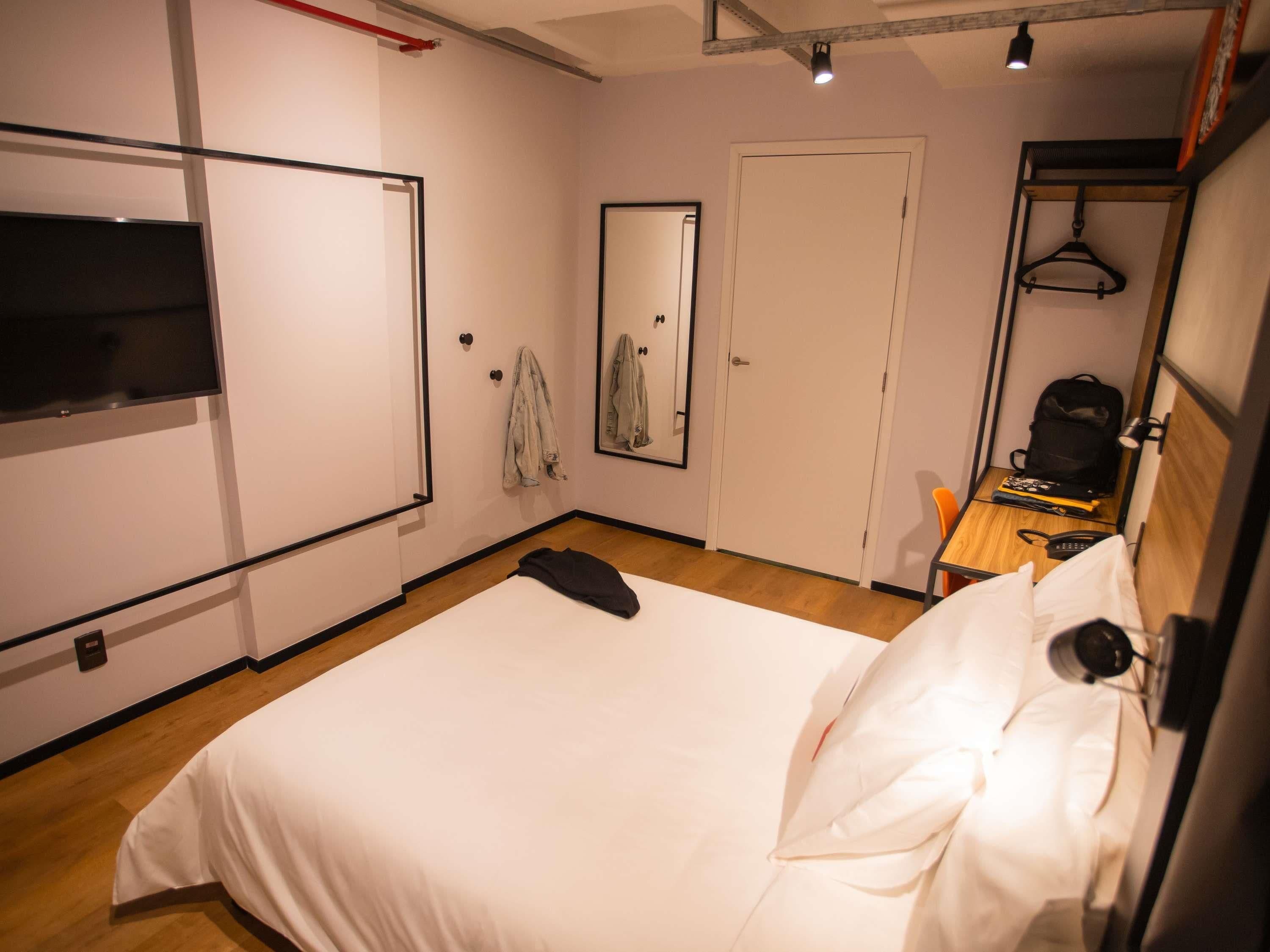 Ein Schlafzimmer mit Bett, Spiegel, Fernseher, Kleiderständer und Schreibtisch mit Stuhl.