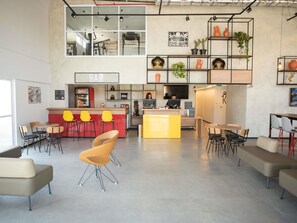 Een moderne bar met een balie, gele stoelen en een zithoek met banken en tafels.