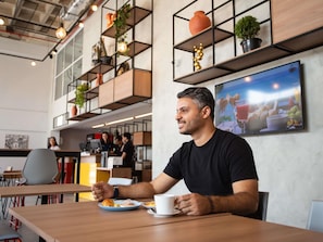A modern cafe with wooden tables and chairs, a counter with staff, and shelves with plants and decorative items. - Ibis Serra Talhada (Serra Talhada)
