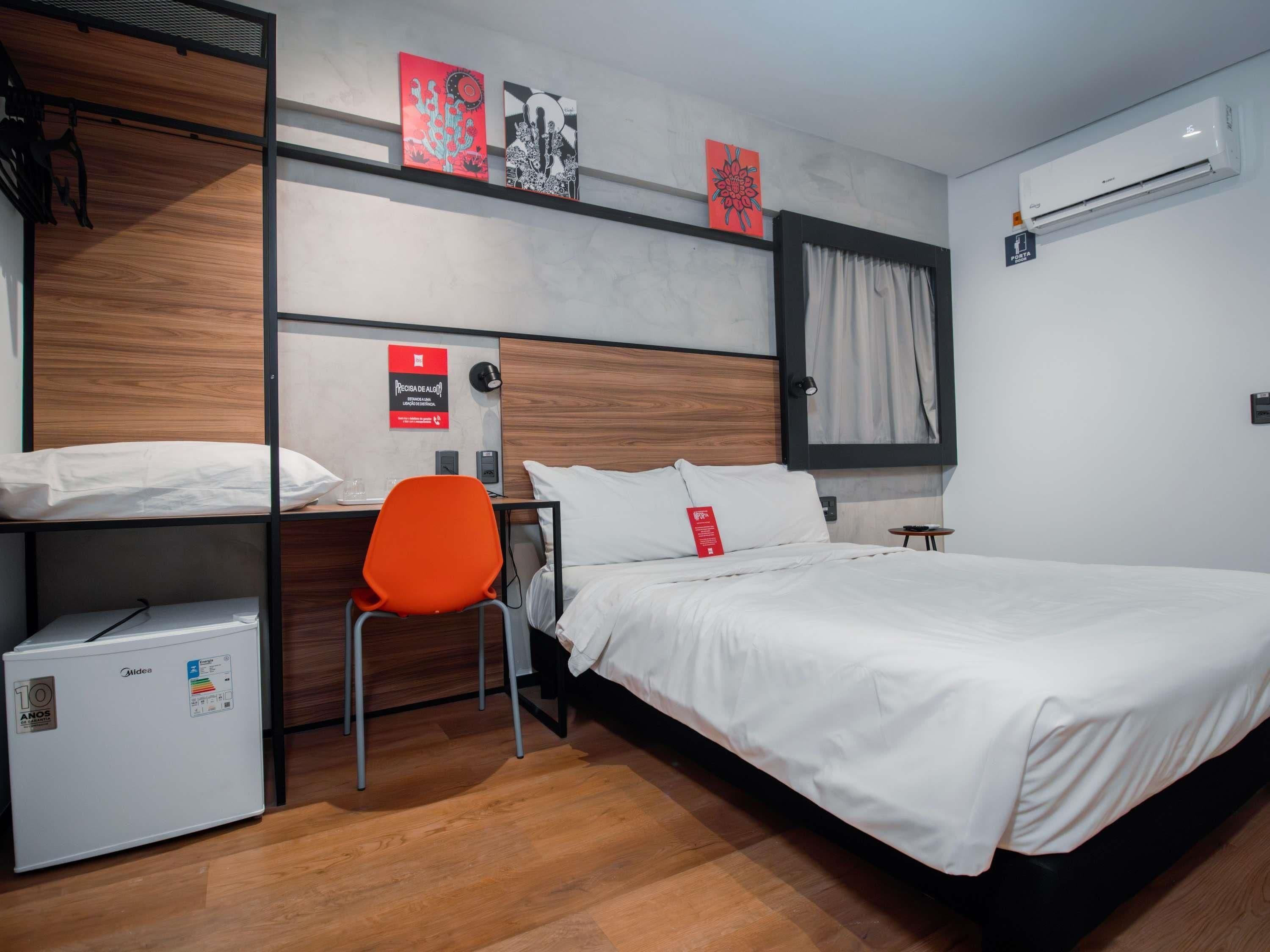 Une chambre d’hôtel équipée d’un lit, d’une chaise, d’un petit réfrigérateur et d’un climatiseur fixé au mur.