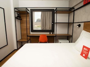 A compact hotel room with a bunk bed, a desk with a chair, a small bedside table, and a window with a view of a mountain. - Ibis Serra Talhada (Serra Talhada)