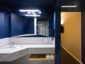 Une salle de bain moderne avec un grand miroir, un lavabo, une douche et un sèche-cheveux.