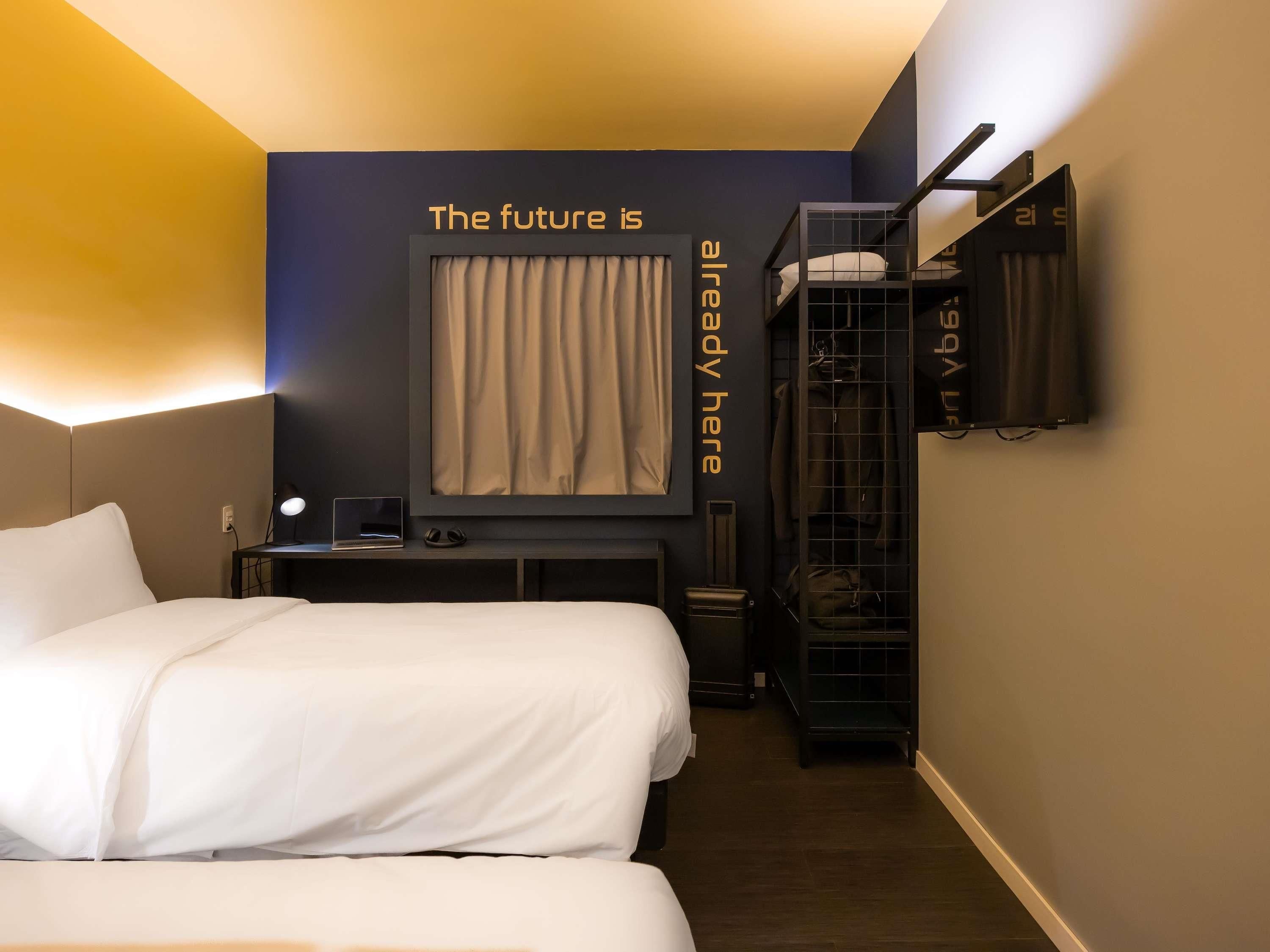A hotel room with a bed, a desk, a chair, a mirror, a wardrobe, and a wall with a text message.
