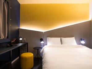 Une chambre d’hôtel avec un lit, un bureau avec un ordinateur portable, un petit tabouret et deux lampes fixées au mur.