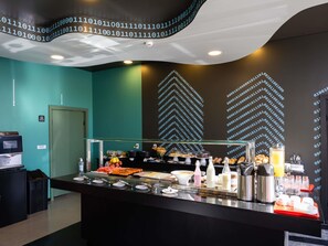 A breakfast buffet with various food items and a digital display of binary code on the wall. - Ibis Styles Barretos (Barretos)