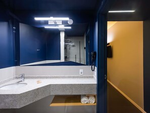 A modern bathroom with a large mirror, a sink, a shower, and a hairdryer.
