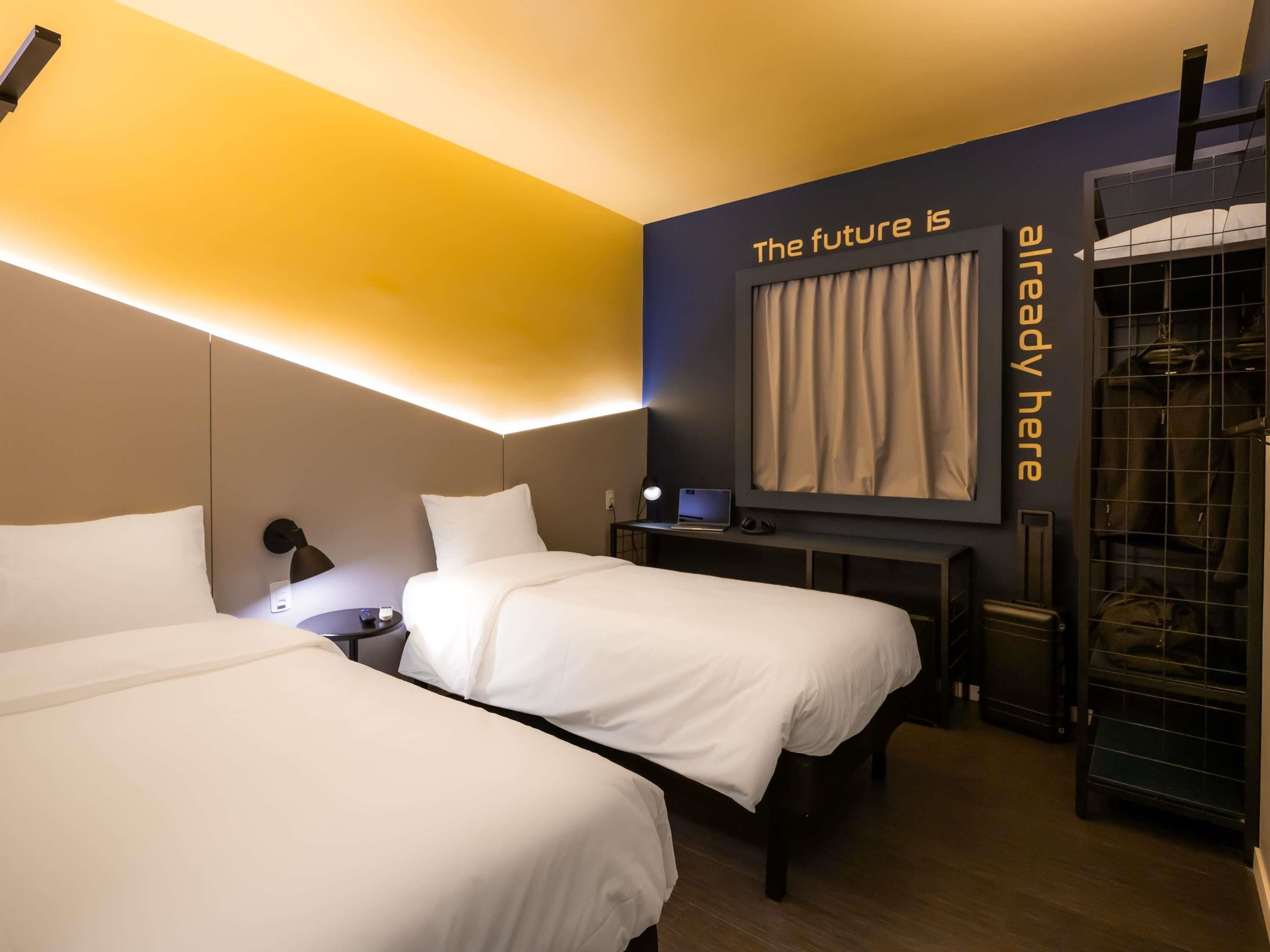 A hotel room with two beds, a desk, a laptop, and a large mirror on the wall.