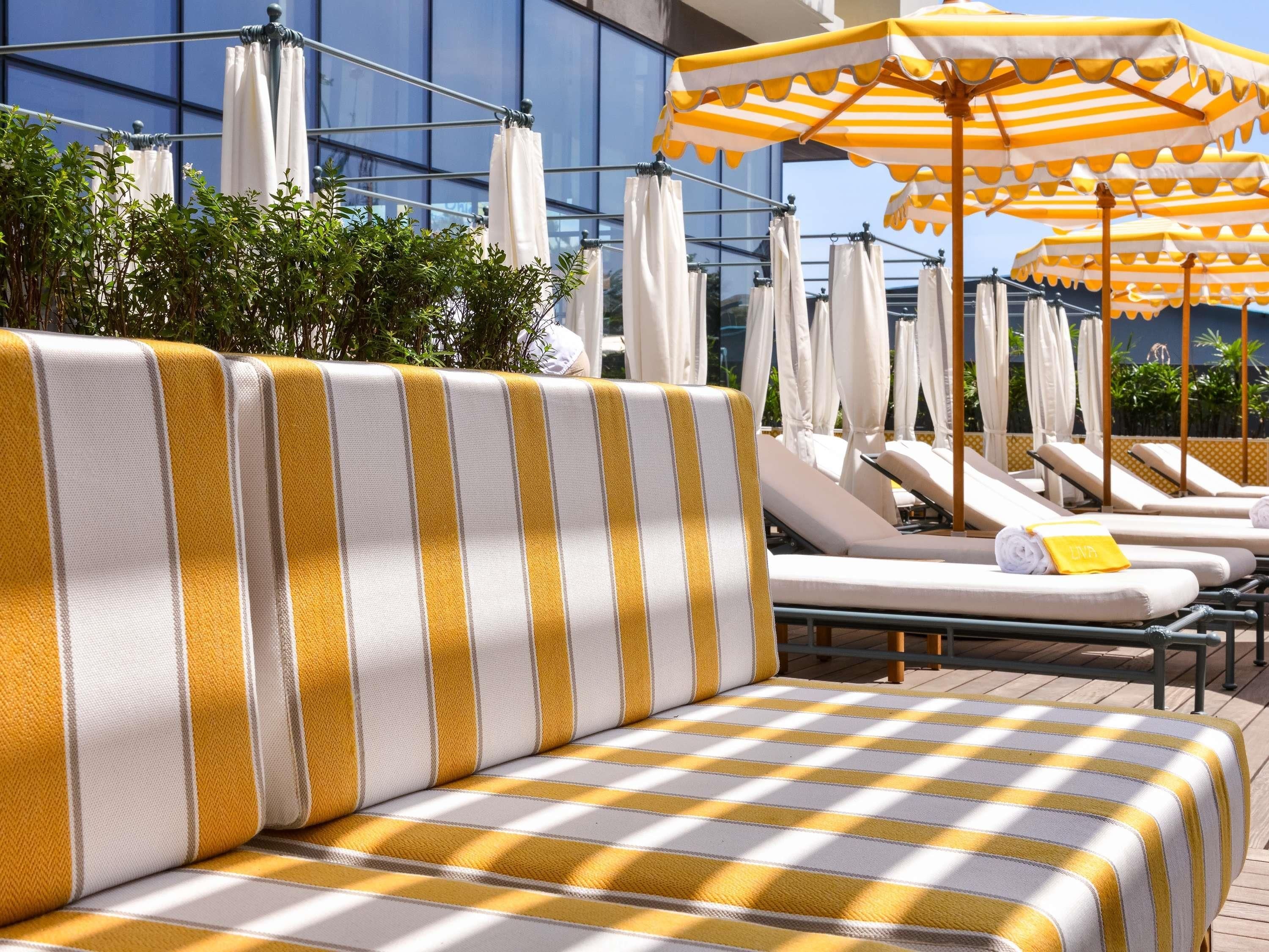 A poolside area with striped lounge chairs, umbrellas, and a modern building in the background.