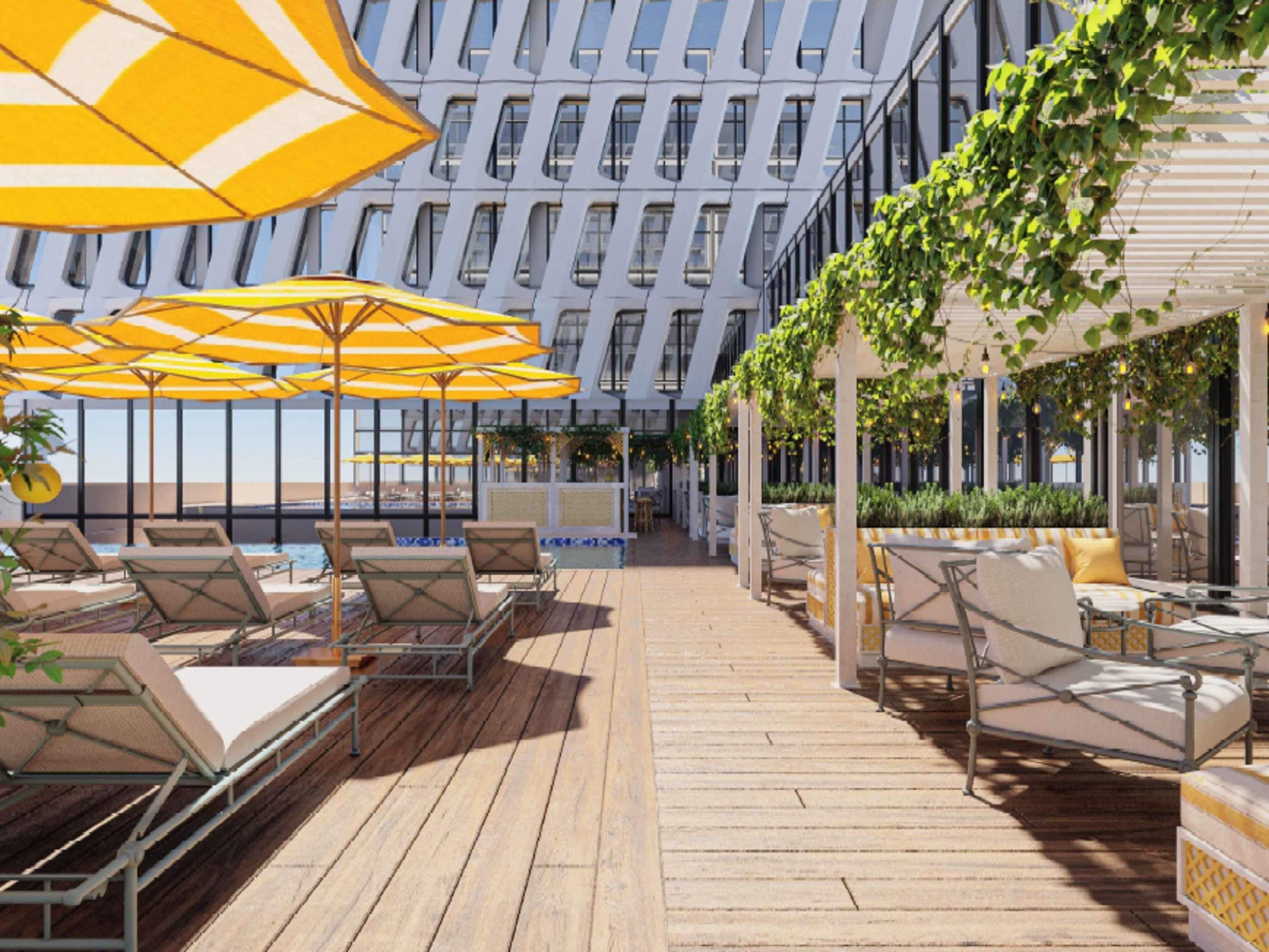 Una terraza en la azotea con mobiliario exterior, sombrillas y un edificio moderno al fondo.
