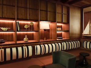 A cozy lounge area with striped sofas, wooden shelves with decorative items, and a small table with a lamp. - Novotel Abidjan Marcory (Abidjan)
