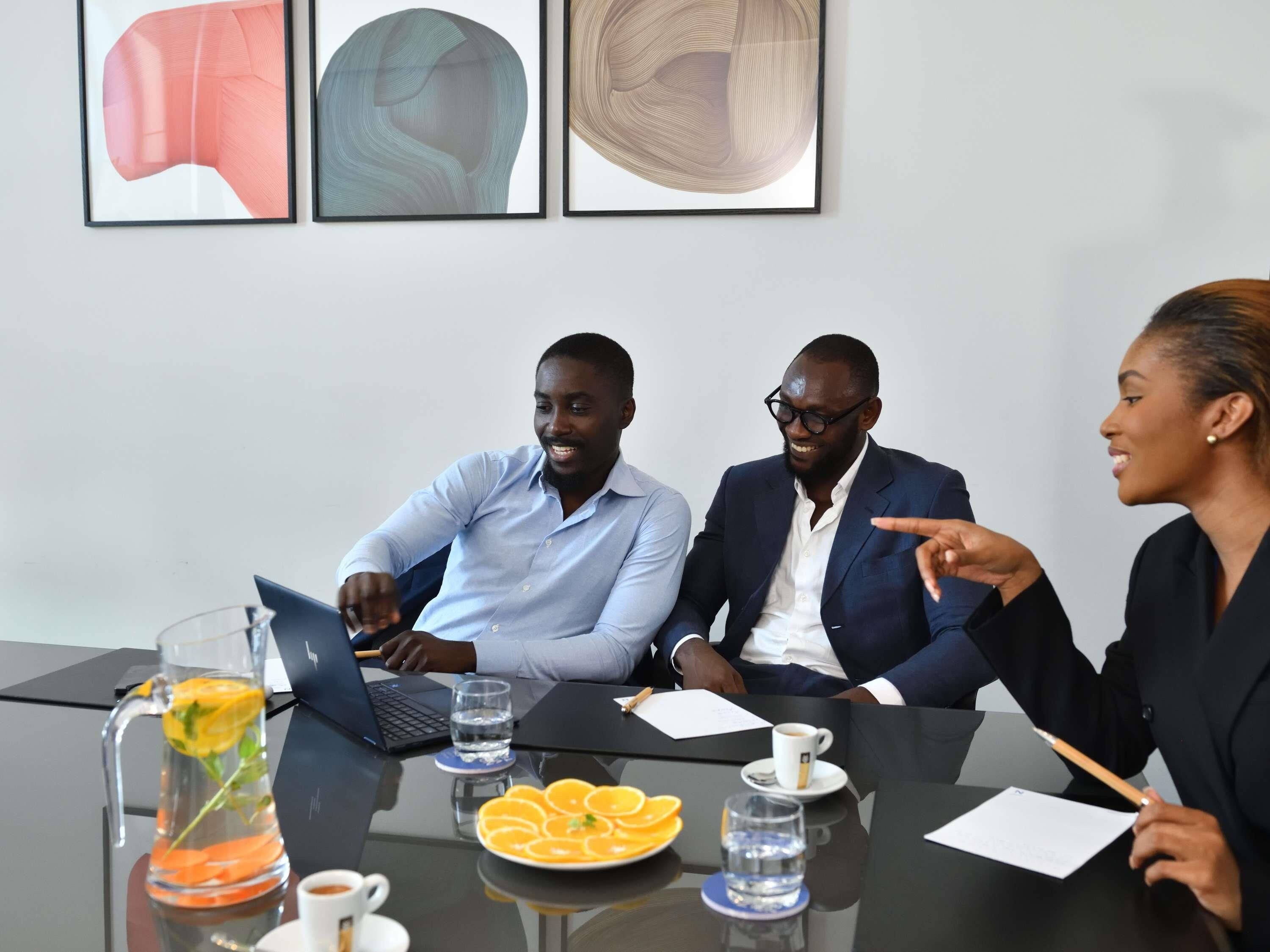 Une salle de réunion avec une table en verre, des ordinateurs portables, des documents et un pichet rempli de tranches d’orange.