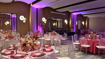 Un salón de banquetes con mesas redondas, sillas transparentes y centros de mesa florales.