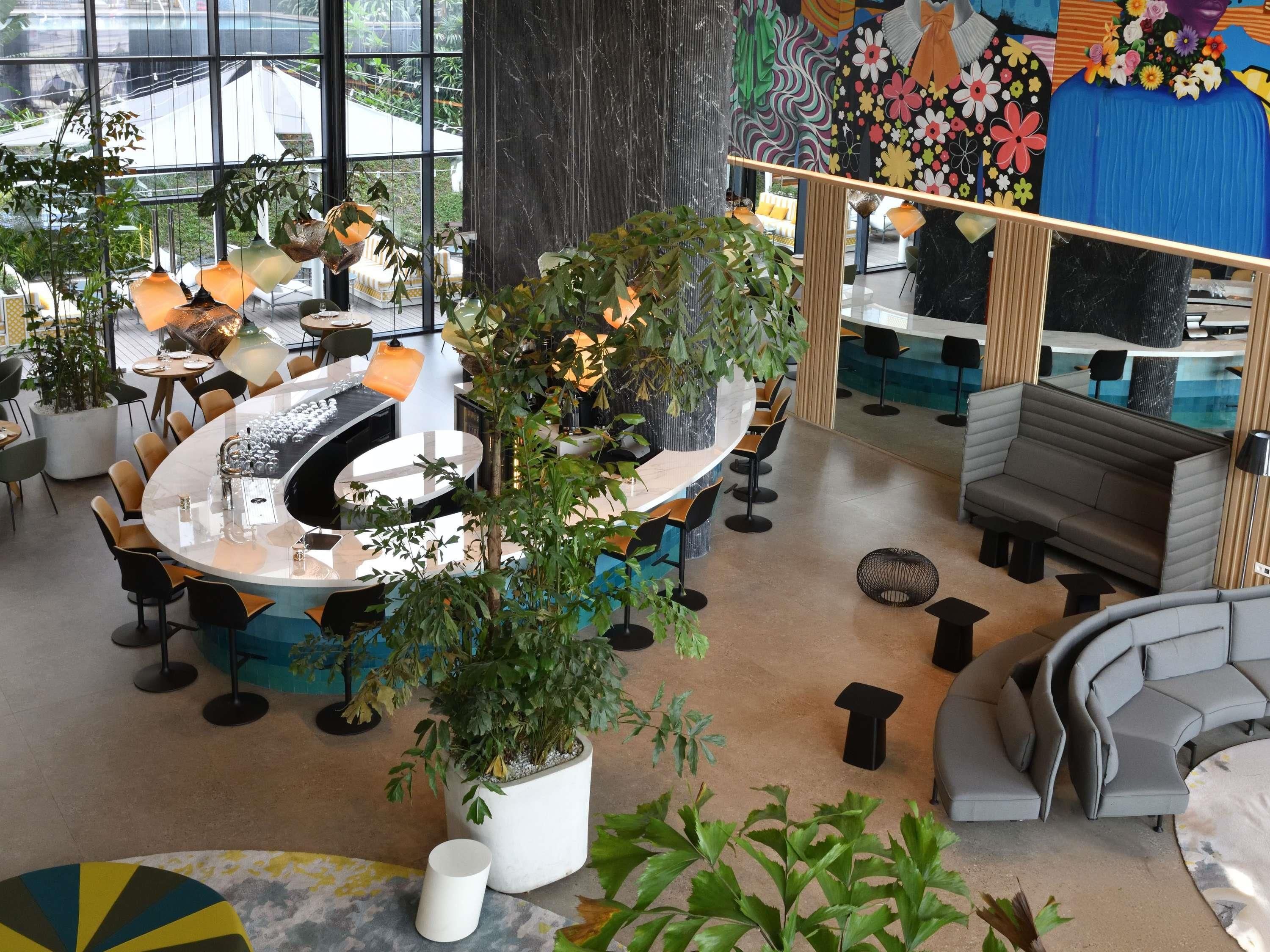 Ein modernes Interieur mit runden Tischen, einer Bar, Sitzgelegenheiten und großen Fenstern.