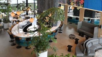 Ein modernes Interieur mit runden Tischen, einer Bar, Sitzgelegenheiten und großen Fenstern.