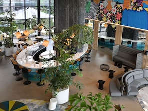 Un interior moderno con mesas redondas, zona de bar, asientos y ventanas amplias.