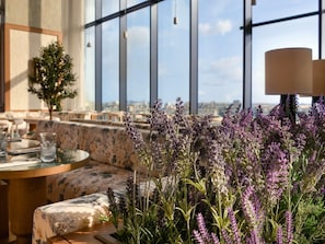 A modern interior with a dining area, a sofa, and a large window with a city view. - Novotel Abidjan Marcory (Abidjan)