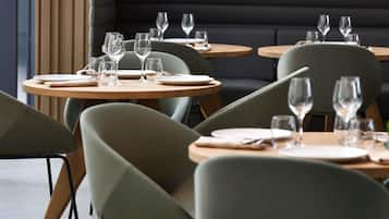 Ein Restaurantinneres mit runden Tischen, grünen Sitzmöglichkeiten und einer dunklen gepolsterten Bank im Hintergrund.