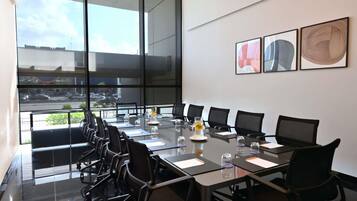 A conference room with a glass table, black chairs, and a city view through large windows.