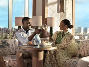 A couple seated at a round table with floral upholstery, a city view, and a lamp in the background. - Novotel Abidjan Marcory (Abidjan)