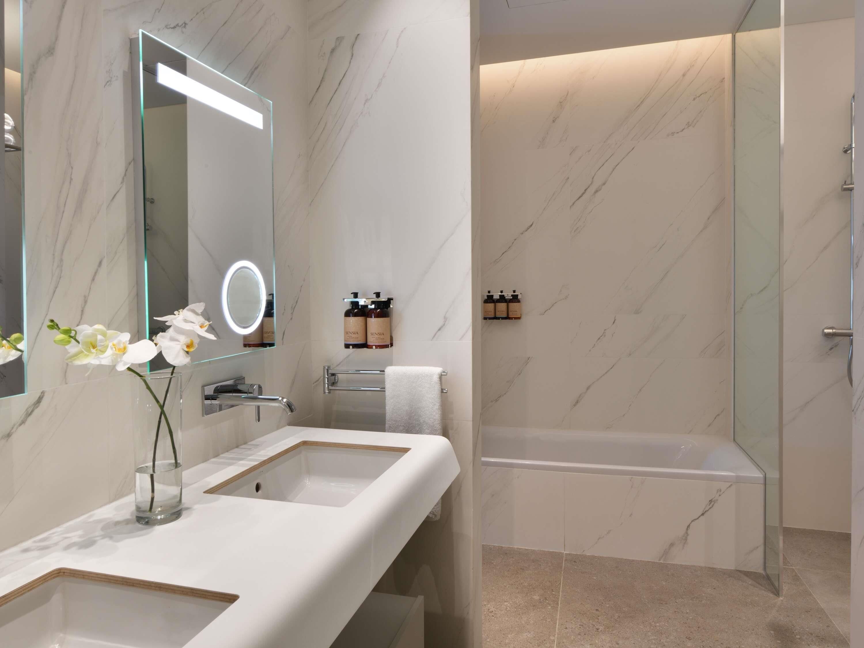 Une salle de bain moderne avec un grand miroir, deux lavabos, une baignoire et une douche.