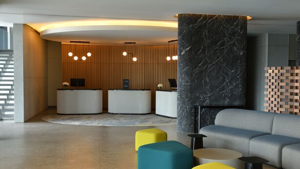 Una moderna zona de recepción con un panel de pared de madera, dos mostradores y un sofá gris.