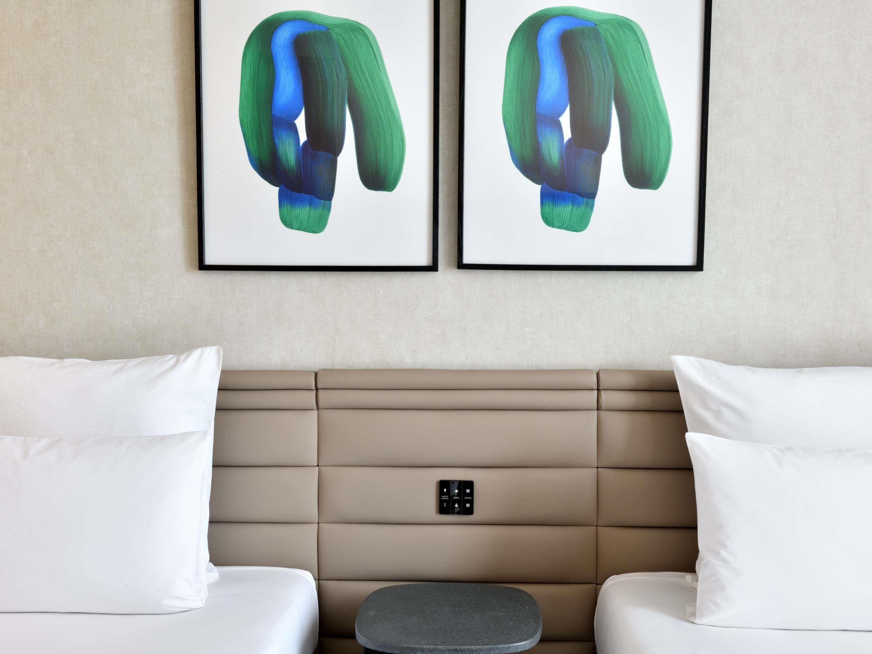 A hotel room with a beige padded headboard, two white pillows, and a small round table.